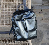 Black metallic backpack on a woven chair with a stone wall background