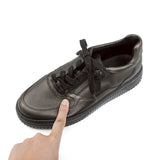Black leather shoe with a finger pointing at it on a white background