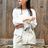 Woman holding Trero Bucket Taupe 2 ways bag against a wooden background