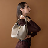 Woman holding a Trero Bucket Taupe handbag against a brown background