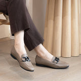 Person wearing brown loafers with decorative buckles on a wooden floor.