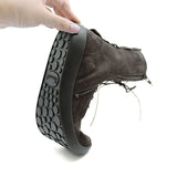 A hand is holding a dark brown suede ankle boot with a thick black sole, showing the tread pattern and the 'Think!' brand logo embossed on the side of the sole, against a white background.